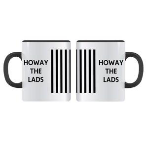 Op de afbeelding: Twee witte keramische mokken met zwarte handvatten. De ene mok heeft de tekst "HOWAY THE LADS" aan de linkerkant en zwarte verticale strepen aan de rechterkant. De andere mok heeft de tekst "HOWAY THE LADS" aan de rechterkant en zwarte verticale strepen aan de linkerkant.