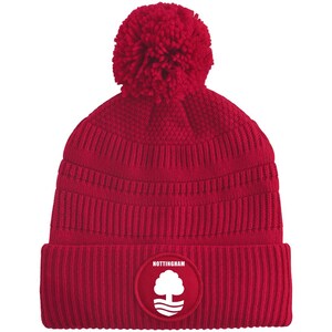 May include: A red knit beanie with a large pom-pom on top. The hat features a ribbed brim and a circular patch with the word "NOTTINGHAM" and a white tree logo. The hat is made of a soft, warm material.