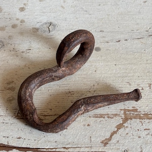 May include: A rusty metal hook with a loop at the top. The hook is bent into a curved shape and has a pointed end.