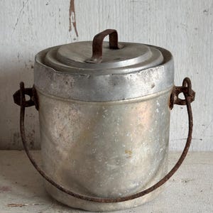 Oude aluminium kookpot met gebogen handvat en deksel.