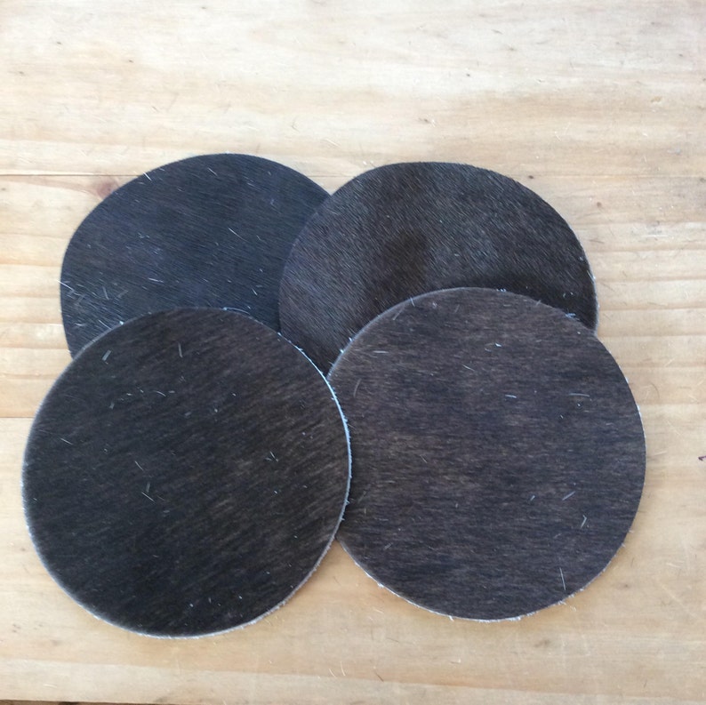 May include: Four dark brown cowhide coasters with a fuzzy texture.