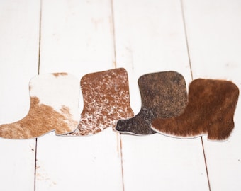 May include: Four cowhide boot shapes in different colors and patterns. The boots are brown, white, black, and brown with white spots.