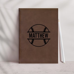 May include: Brown leather journal with a black baseball graphic and the name "MATTHEW" printed on a white banner.