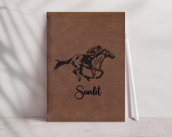 May include: A brown leather journal with a black silhouette of a horse and rider. The name "Scarlet" is written in cursive below the image.