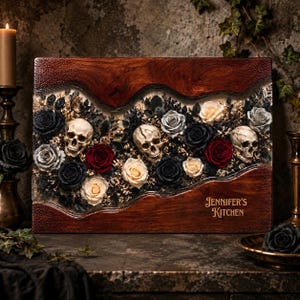 May include: A rectangular wooden cutting board featuring a central resin inlay filled with preserved black, red, and cream roses, dried foliage, and three realistic human skulls. The text "JENNIFER'S KITCHEN" is engraved on the bottom right corner.