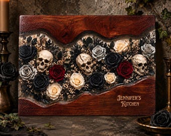 May include: A rectangular wooden cutting board featuring a central resin inlay filled with preserved black, red, and cream roses, dried foliage, and three realistic human skulls. The text "JENNIFER'S KITCHEN" is engraved on the bottom right corner.