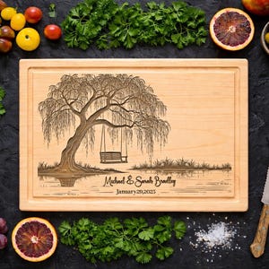 May include: A rectangular wooden cutting board with a carved tree and swing design. The text "Michael & Sarah Bradley January 20, 2025" is engraved below the tree. The board is surrounded by fresh produce, including tomatoes, grapes, and oranges.