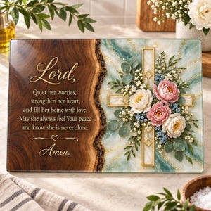 May include: A rectangular glass plaque featuring a wood grain design on the left with the text: Lord, Quiet her worries, strengthen her heart, and fill her home with love. May she always feel Your peace and know she is never alone. Amen. The right side displays a gold-trimmed cross adorned with pink and white flowers and green leaves over a teal and white marble pattern.