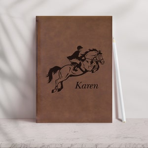 Pu&ograve; includere: Diario in pelle marrone con una silhouette nera di una persona a cavallo che salta un ostacolo. Il nome "Karen" &egrave; inciso sotto l'immagine.