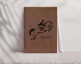 May include: Brown leather journal with a black silhouette of a person riding a horse jumping over a fence. The name "Karen" is engraved below the image.