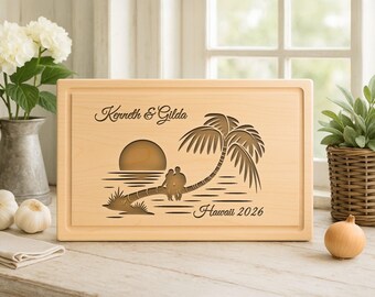 Op de afbeelding: Een rechthoekige houten snijplank met een gegraveerde tropische scène. Het ontwerp omvat een palmboom, zonsondergang en silhouetten van een stel. De namen "Kenneth & Gilda" en "Hawaii 2026" zijn ook gegraveerd.