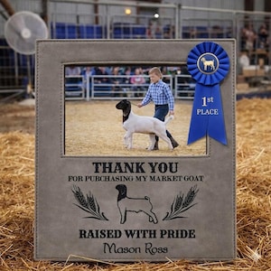 May include: A gray picture frame with a photo of a person leading a goat. The frame has text that reads "THANK YOU FOR PURCHASING MY MARKET GOAT" and "RAISED WITH PRIDE". A blue ribbon with "1st PLACE" is attached.
