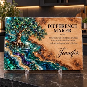 May include: A rectangular glass plaque featuring a wood grain background and a vibrant resin art design of a tree over a flowing river in shades of teal, blue, and purple. The text reads: DIFFERENCE MAKER noun Someone whose kindness inspires, whose dedication lifts others, and whose impact lasts a lifetime. see also: Jennifer.