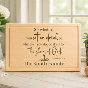 May include: A rectangular wooden cutting board with a carved border. The board features the text "So whether you eat or drink or whatever you do, do it all for the glory of God." and "The Smith Family."