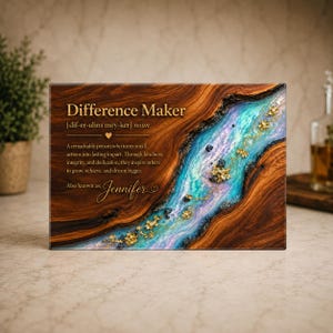 May include: A rectangular wooden plaque featuring a natural wood grain finish and a central resin river in shades of blue, purple, and teal. The text reads Difference Maker, a definition of the term, and the name Jennifer in gold script lettering.