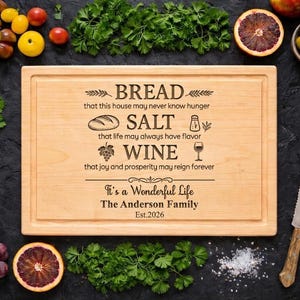 May include: A wooden chopping board with engraved text, surrounded by fresh produce. The text reads "Bread, Salt, Wine" and "It's a Wonderful Life." The board is surrounded by tomatoes, grapes, herbs, and a knife.