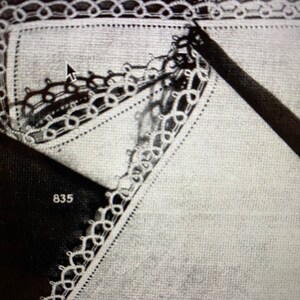 May include: A close-up of a white fabric with a delicate lace trim. The lace is a repeating pattern of small loops and circles. The number 835 is visible in the lower left corner of the image.