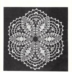 May include: A white crochet doily with a filet and shell design. The doily is circular and has a center with a smaller circle. The doily is on a black background.