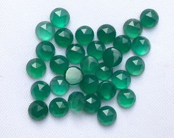 May include: A collection of green gemstone cabochons, each with a faceted, rounded shape. The stones are arranged in a loose pile on a white background.