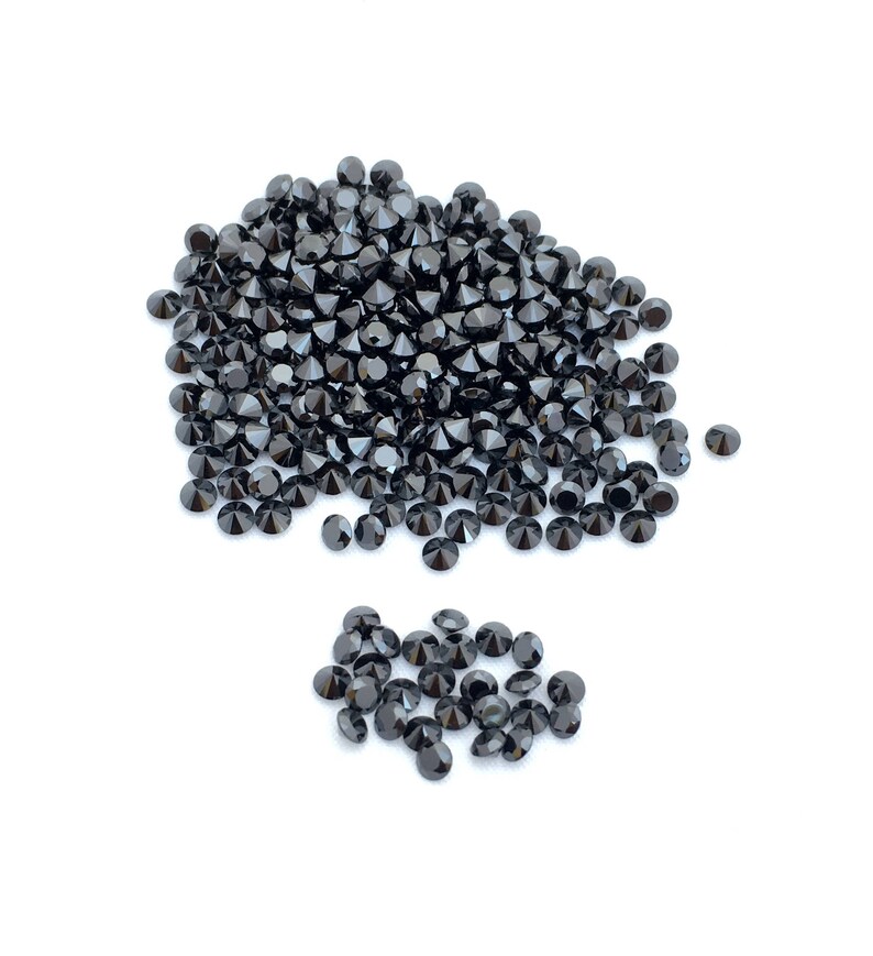 May include: A large pile of black round gemstones, with a smaller pile of black round gemstones to the side.