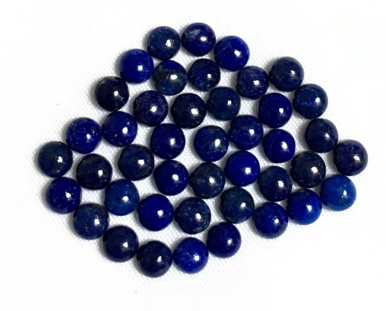 May include: A collection of 40 round, dark blue lapis lazuli gemstone cabochons. The cabochons are smooth and polished.