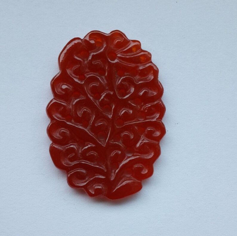 K&ouml;nnte beinhalten: Ein roter, geschnitzter Steinanh&auml;nger in Form eines Baumes mit filigranen Details.