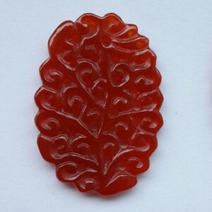 K&ouml;nnte beinhalten: Ein roter, geschnitzter Steinanh&auml;nger in Form eines Baumes mit filigranen Details.