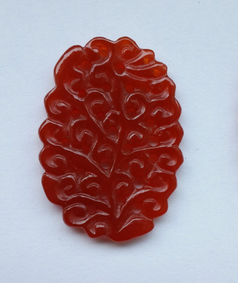 K&ouml;nnte beinhalten: Ein roter, geschnitzter Steinanh&auml;nger in Form eines Baumes mit filigranen Details.