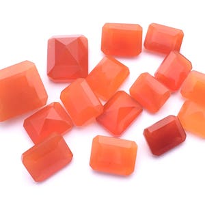 Puede incluir: Una colecci&oacute;n de 13 piedras preciosas de cornalina naranja, talladas en forma rectangular. Las piedras est&aacute;n dispuestas sobre un fondo blanco.