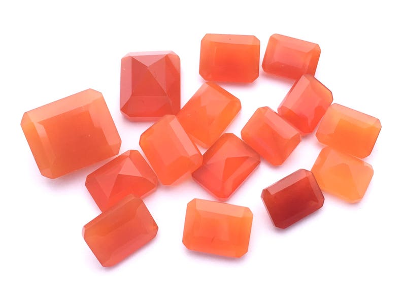 Puede incluir: Una colecci&oacute;n de 13 piedras preciosas de cornalina naranja, talladas en forma rectangular. Las piedras est&aacute;n dispuestas sobre un fondo blanco.