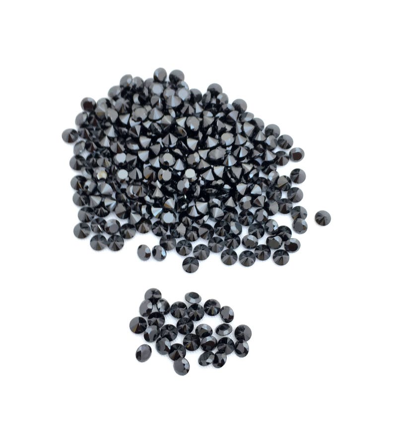 May include: A large pile of black round gemstones, with a smaller pile of black round gemstones to the side.
