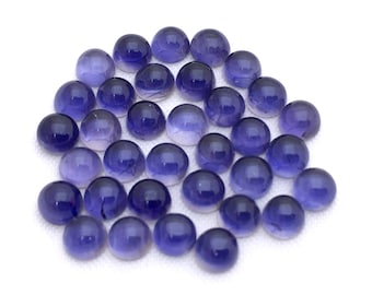 May include: A collection of round, purple gemstones, also known as amethyst, arranged in a loose pile. The gemstones are smooth and polished, with a slight sheen.
