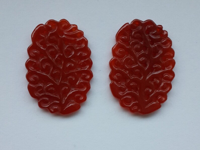 K&ouml;nnte beinhalten: Zwei rote Karneol-Anh&auml;nger mit einem komplizierten geschnitzten Blumenmuster.