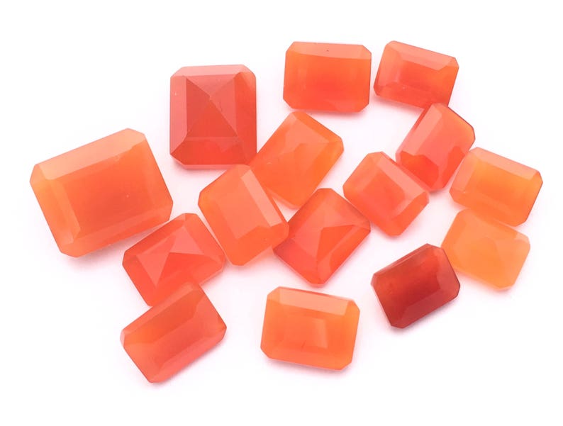 Puede incluir: Una colecci&oacute;n de 13 piedras preciosas de cornalina naranja, talladas en forma rectangular, presentadas sobre un fondo blanco.