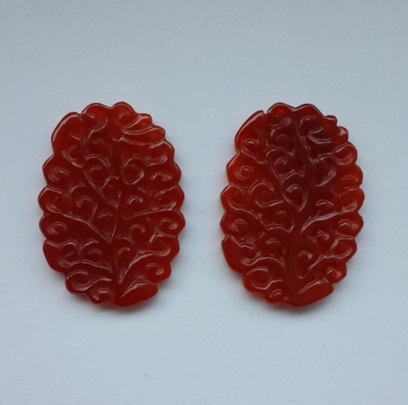 K&ouml;nnte beinhalten: Zwei rote Karneol-Anh&auml;nger mit einem komplizierten, in die Oberfl&auml;che geschnitzten Blumenmuster.