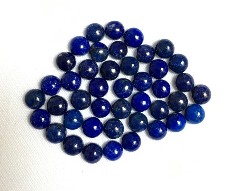 May include: A collection of round, dark blue lapis lazuli gemstone beads. The beads are smooth and polished, and they are arranged in a loose pile.