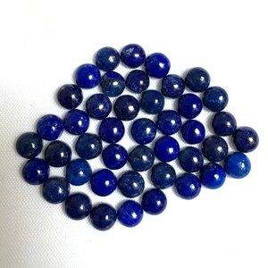 May include: A collection of round, dark blue lapis lazuli gemstone cabochons. The cabochons are smooth and polished, with a slight shimmer.