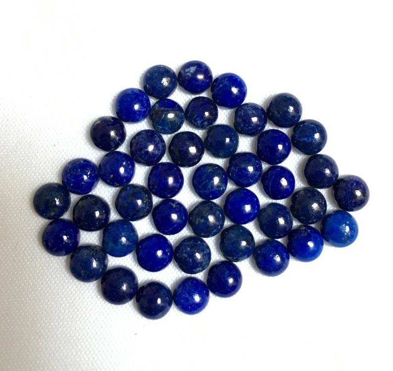 May include: A collection of round, dark blue lapis lazuli gemstone cabochons. The cabochons are smooth and polished, with a slight shimmer.