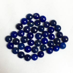 May include: A collection of round, dark blue lapis lazuli cabochons. The cabochons are smooth and polished, with a slight variation in size and shape.
