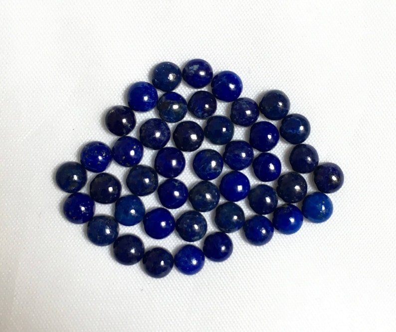 May include: A collection of round, dark blue lapis lazuli cabochons. The cabochons are smooth and polished, with a slight variation in size and shape.