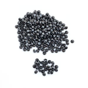 May include: A large pile of black round gemstones, with a smaller pile of the same gemstones to the side.