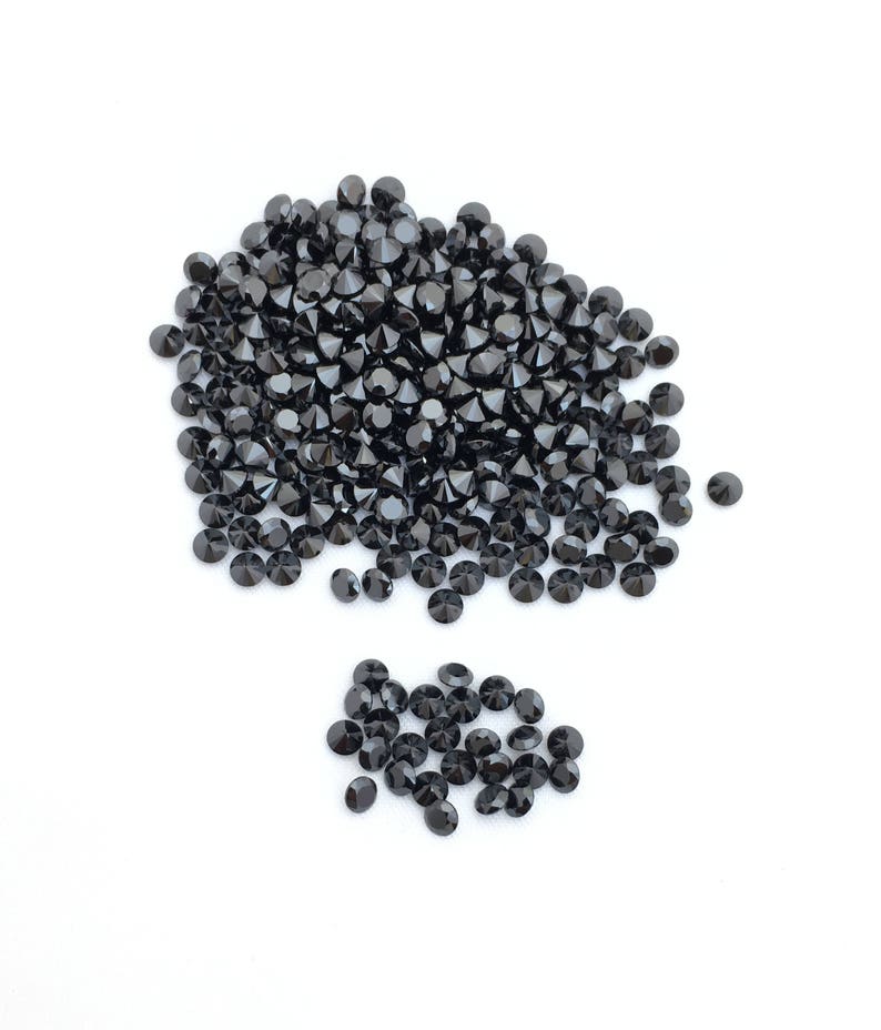May include: A large pile of black round gemstones, with a smaller pile of the same gemstones to the side.