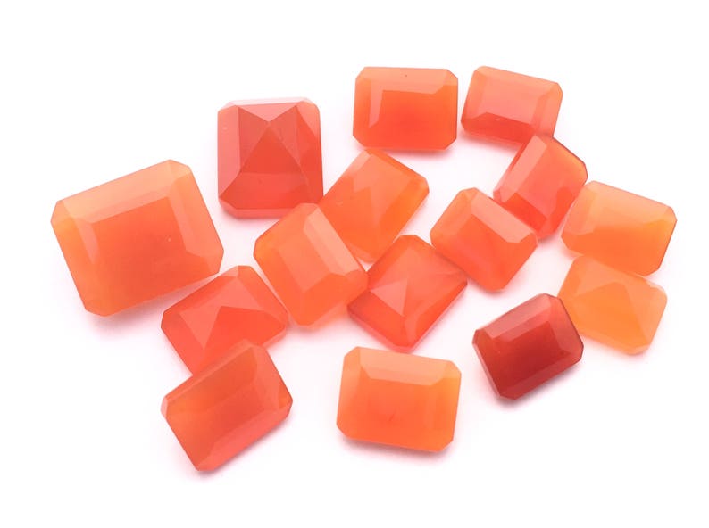 Puede incluir: Una colecci&oacute;n de 14 piedras preciosas de cornalina naranja, talladas en forma rectangular, presentadas sobre un fondo blanco.