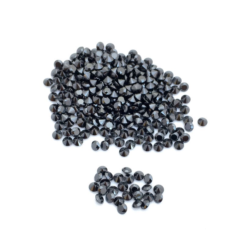 May include: A large pile of black round gemstones, with a smaller pile of black round gemstones to the side.
