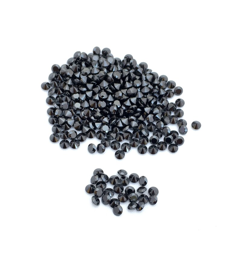May include: A large pile of black round gemstones, with a smaller pile of black round gemstones to the side.