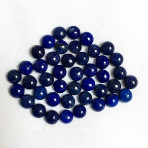 May include: A collection of round, dark blue lapis lazuli gemstone beads. The beads are smooth and polished, and they are arranged in a loose pile.
