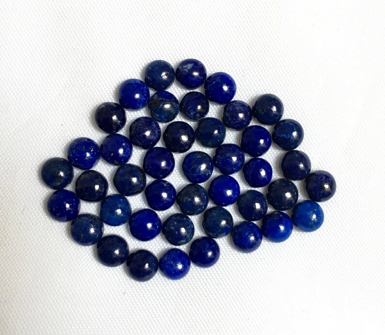 May include: A collection of round, dark blue lapis lazuli gemstone beads. The beads are smooth and polished, and they are arranged in a loose pile.