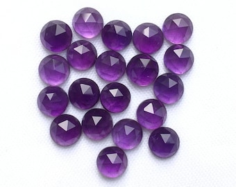 May include: A collection of 20 faceted amethyst gemstones, each with a round shape and a deep purple hue. The stones are arranged in a loose cluster on a white background.