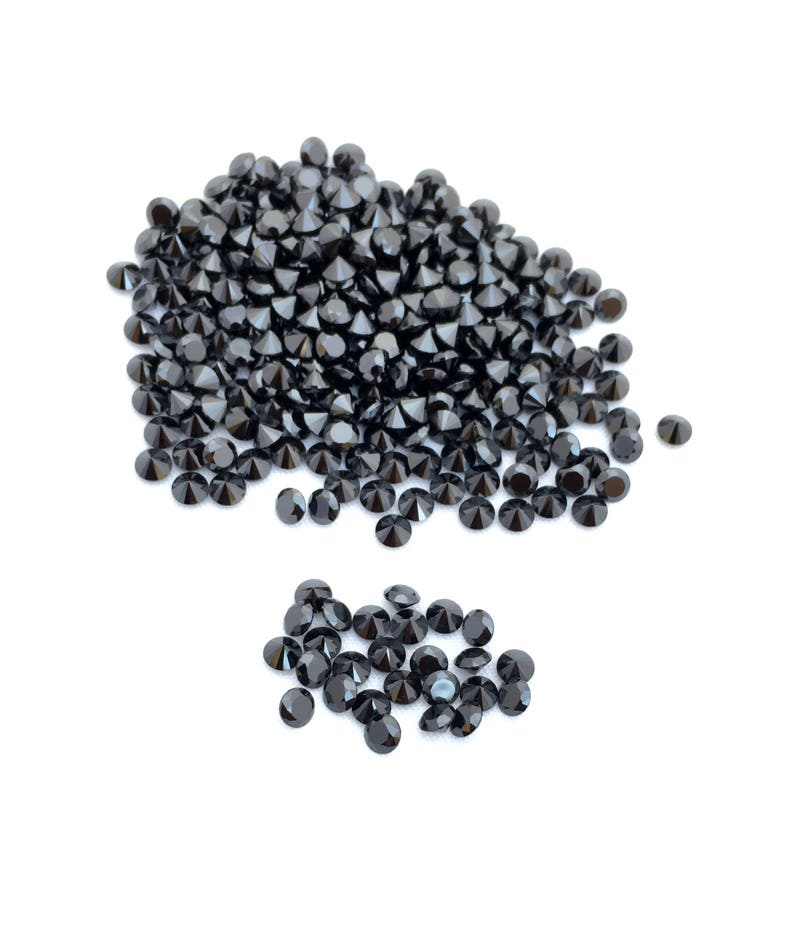 May include: A large pile of black round gemstones, with a smaller pile of black round gemstones to the side.