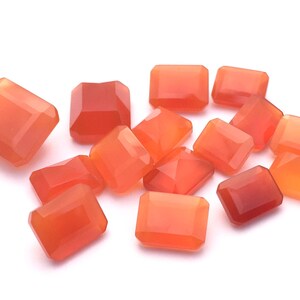 Puede incluir: Una colecci&oacute;n de 14 piedras preciosas de cornalina naranja, talladas en forma rectangular. Las piedras preciosas est&aacute;n dispuestas en un mont&oacute;n suelto sobre un fondo blanco.